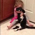Niña graciosa abraza sin mesura a su gato, que está harto de ella